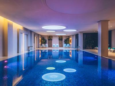 Illuminated indoor pool with round ceiling lights and seating areas along the sides.
