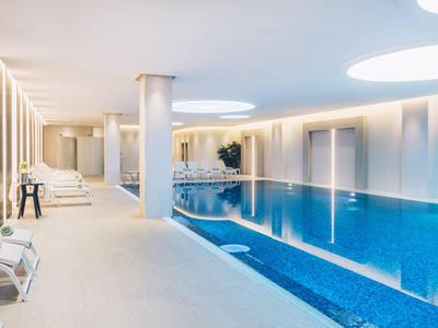 Modern indoor pool with blue water, white walls, and relaxing lounge chairs.