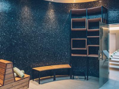 Modern spa room with bench and shelves against dark wall under ceiling lights.