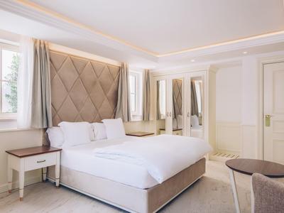 Helles Schlafzimmer mit großem Bett, weißer Bettwäsche, hellen Möbeln und großem Spiegel.