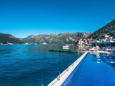 Infinity pool overlooking sea and mountains under clear sky.