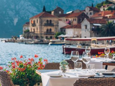 Restaurant terrace with set tables overlooking water and mountain village