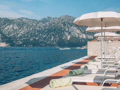 Lounge chairs with white umbrellas by the water with mountains in the background.