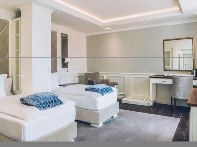 Modern hotel room with two single beds, desk, and carpeted floor.