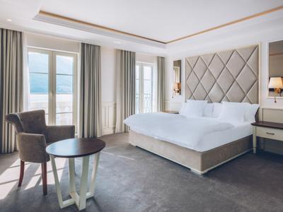 Bright hotel room with large bed, seating area, and sea view.