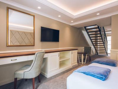 Bright hotel room with desk, TV, and stairs to an upper floor.