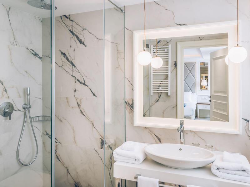 Bright bathroom with marble walls, large mirror, and modern shower.