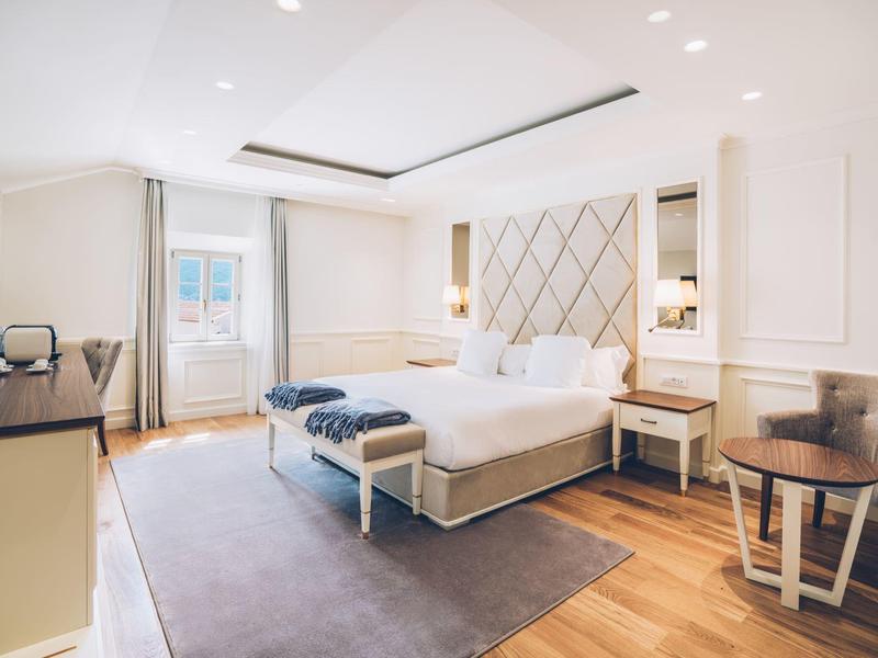 Bright, modern hotel room with large double bed, seating area, and wooden floor.