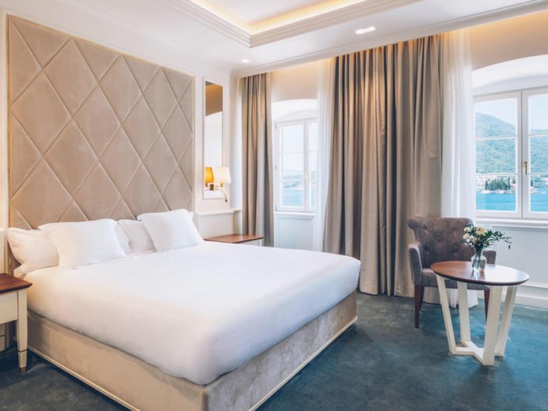 Modern hotel room with large bed, seating area, and water view