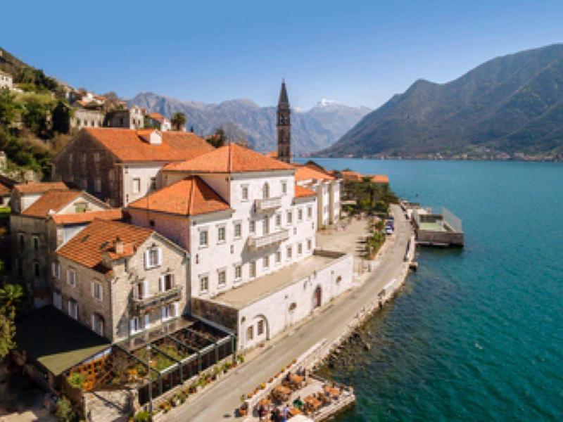 Old town with red roofs by the water against mountains and clear blue sky.