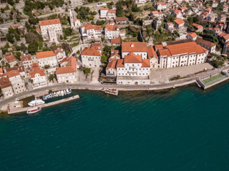 Aerial view of a historic coastal town with red roofs and fishing boats on the water.