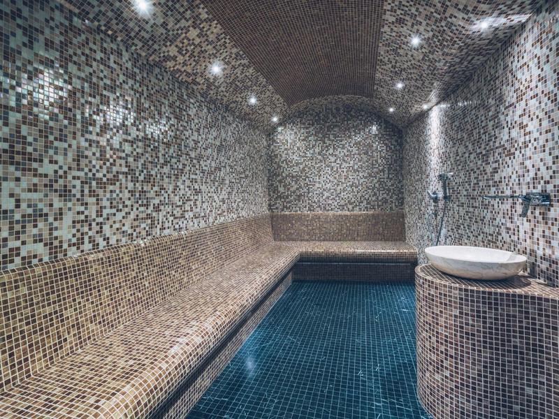 Modern indoor pool with mosaic tiles and indirect lighting.