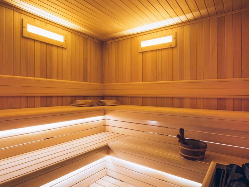 Bright, modern sauna with wooden walls and benches, including bucket and ladle.