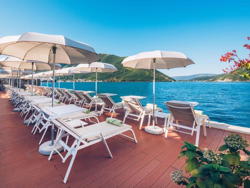 Sunny terrace with loungers and white umbrellas by the blue sea.