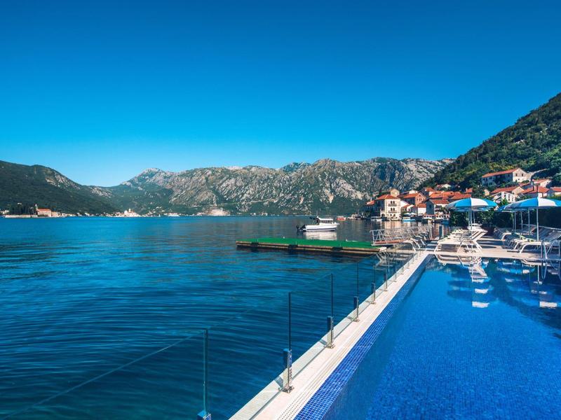 Infinity pool overlooking sea and mountains under clear sky.