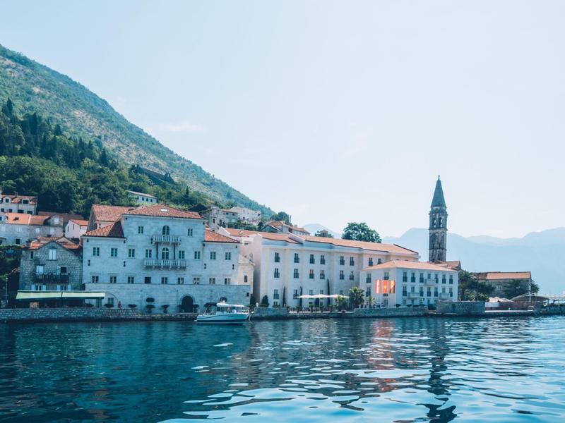 Coastal town with historic buildings and bell tower by calm water under clear sky.