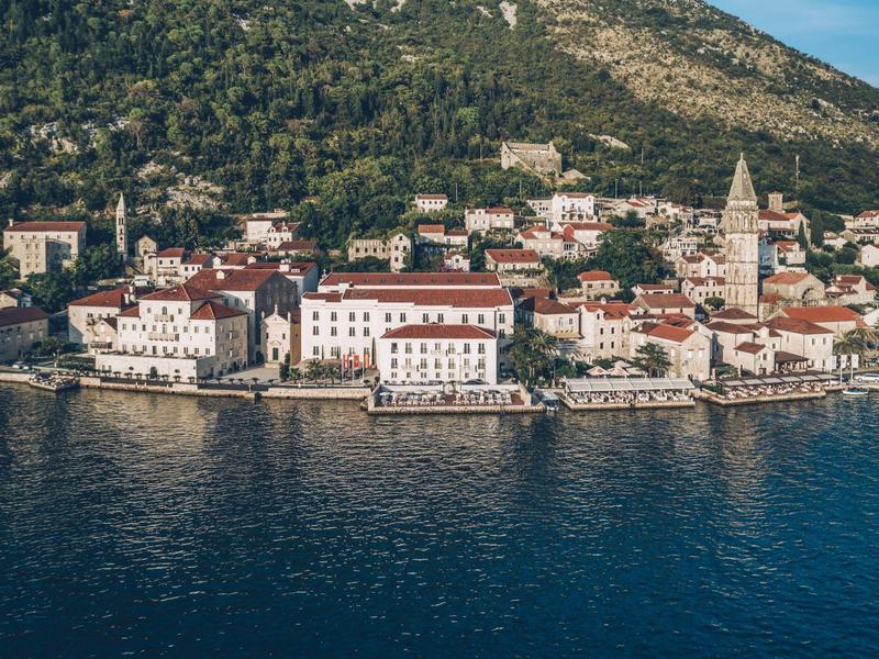 Coastal town with historic buildings by the water and forested hill in the background