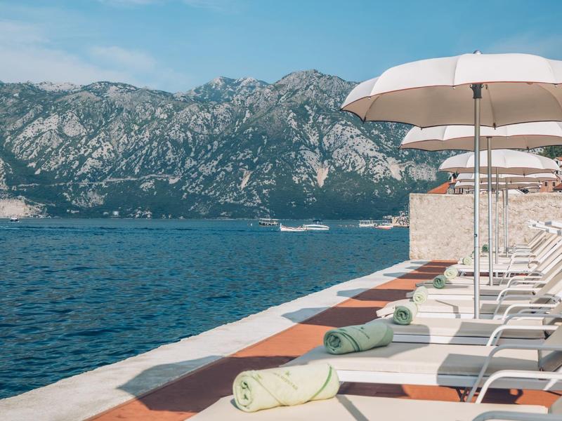 Lounge chairs with white umbrellas by the water with mountains in the background.