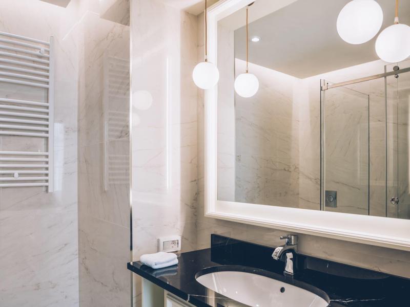 Modern hotel bathroom area with illuminated mirror and glass shower.