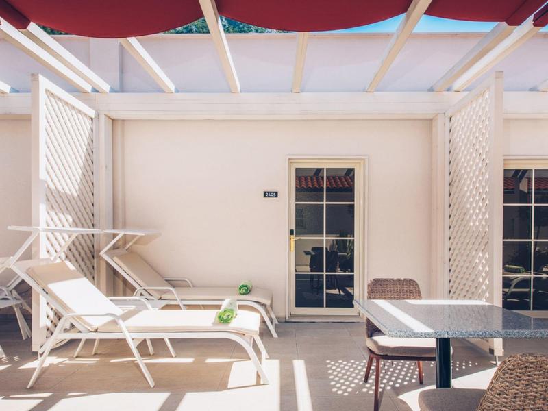 Bright terrace with two lounge chairs, small table, and sunshade on the hotel balcony.