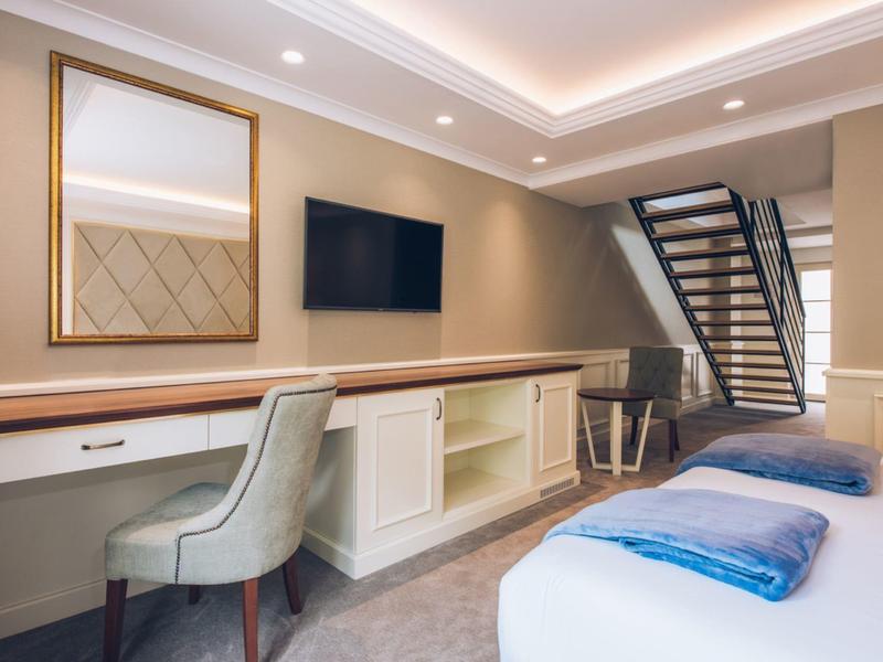 Bright hotel room with desk, TV, and stairs to an upper floor.