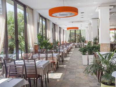 Hell beleuchteter Speisesaal mit Reihen von gedeckten Tischen und Stühlen, dekoriert mit Pflanzen.