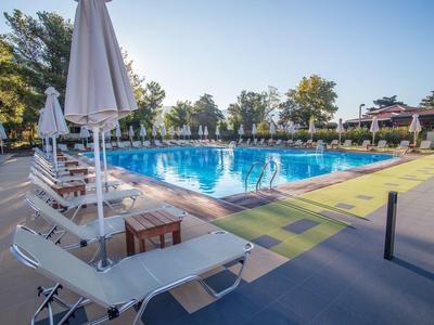 Leerer Poolbereich mit Sonnenliegen und weißen Sonnenschirmen an einem sonnigen Tag