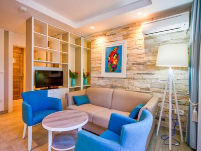 Modern eingerichtetes Wohnzimmer mit Sofa, blauen Sesseln und Fernseher in einem Hotelzimmer.