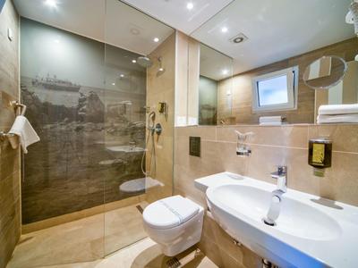 Modernes Badezimmer mit Glasdusche, Toilette, Waschbecken und beiger Fliesenwand