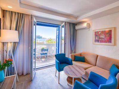 Helles Hotelzimmer mit Sitzbereich, Sofa und Balkon mit Meerblick.