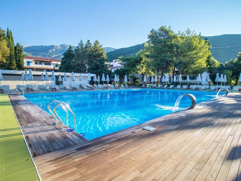 Schwimmbad mit klarem blauen Wasser, umgeben von Holzdeck und Sonnenschirmen im Hotelbereich.