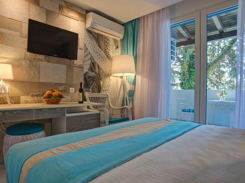 Modernes Hotelzimmer mit Bett, Schreibtisch, Stuhl, TV und Balkon mit Blick auf Bäume.