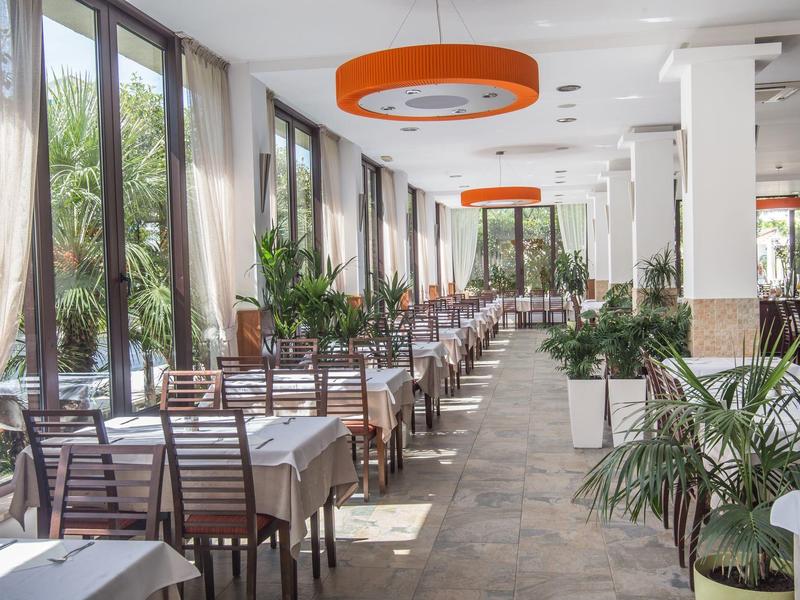 Hell beleuchteter Speisesaal mit Reihen von gedeckten Tischen und Stühlen, dekoriert mit Pflanzen.