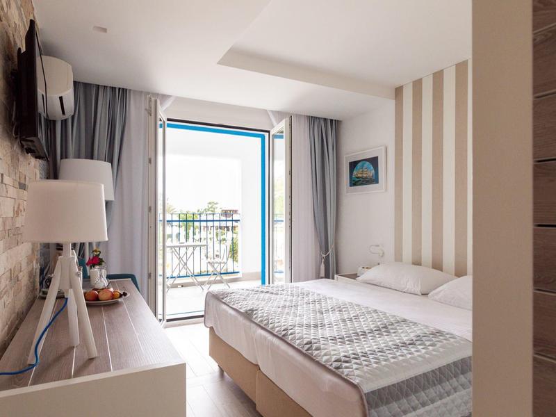 Helles Hotelzimmer mit Doppelbett, Nachttisch, Lampe und Balkon mit Meerblick.