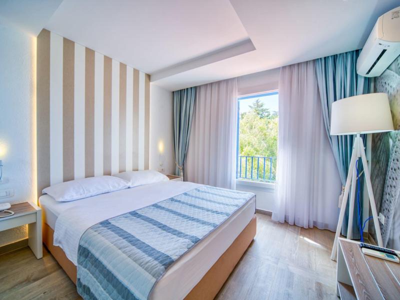 Hell eingerichtetes Hotelzimmer mit Doppelbett, großen Fenstern und moderner Dekoration.