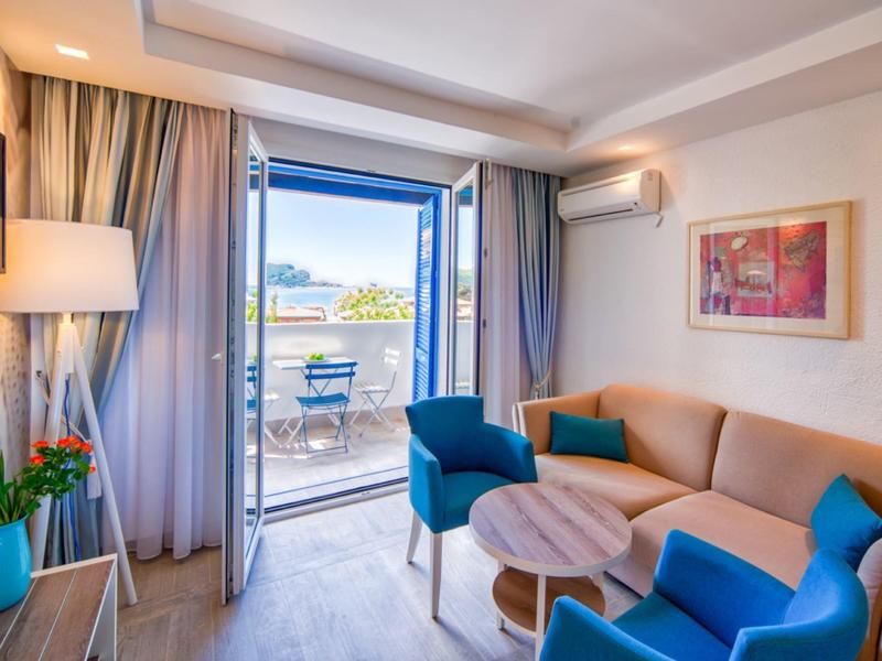 Helles Hotelzimmer mit Sitzbereich, Sofa und Balkon mit Meerblick.