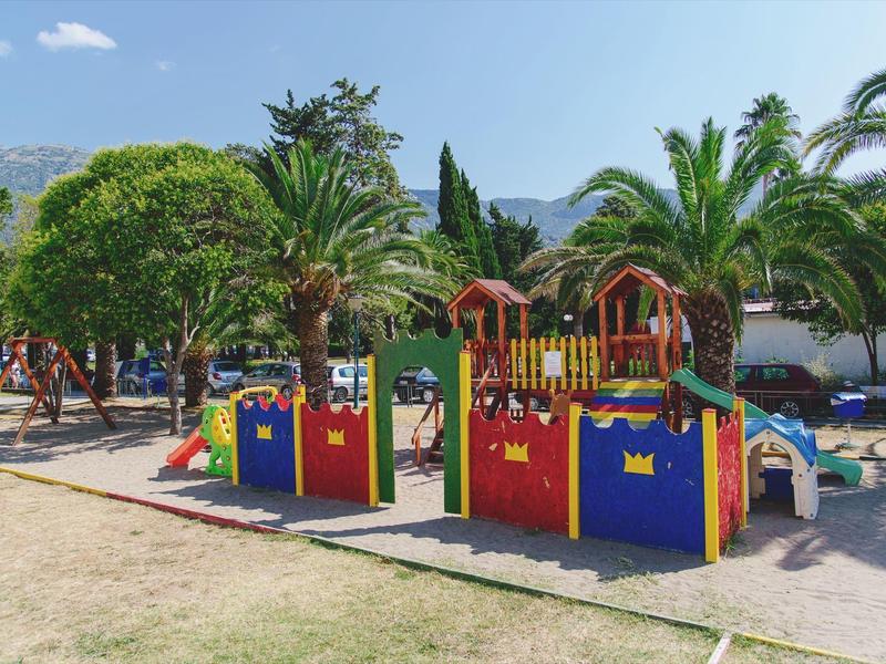 Bunter Spielplatz mit Rutschen, Klettergerüsten und Palmen unter blauem Himmel.