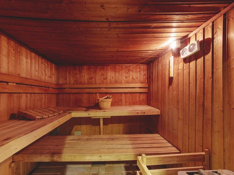Holzsauna mit Bänken, Holzeimer und Aufgussgerät an der Wand, warmes Licht strahlt gemütlich.