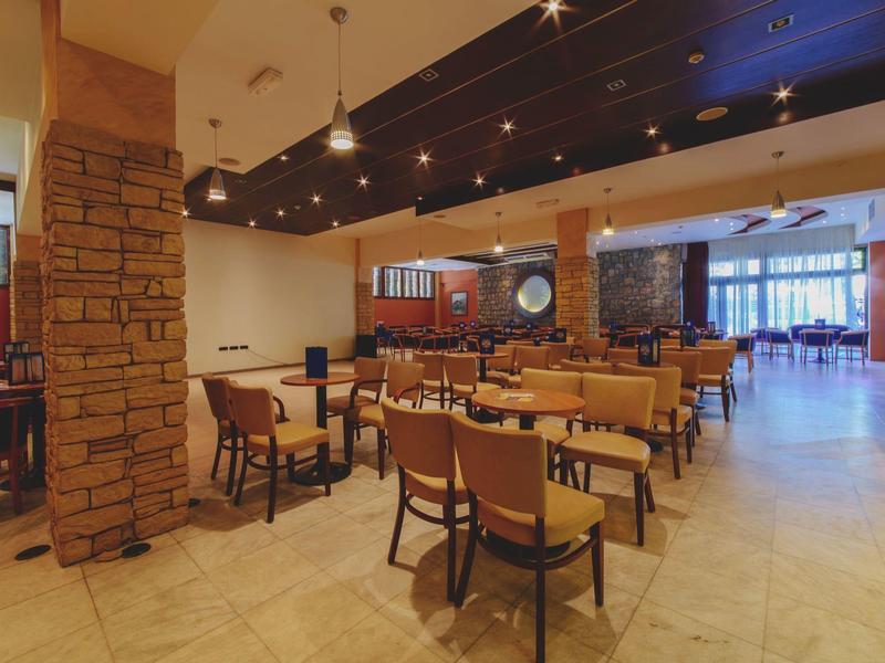 Moderner Gastraum mit Holzmöbeln, Steinsäule, warmem Licht und großen Fenstern im Hintergrund.