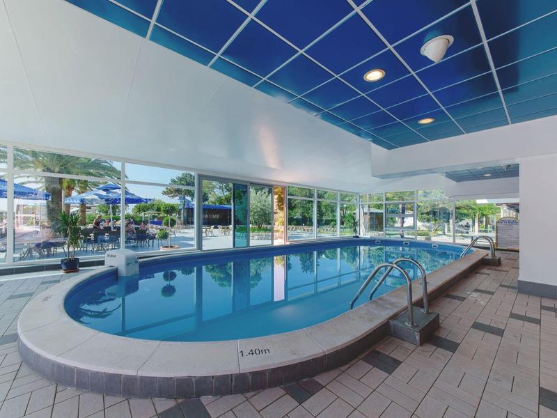 Moderner Innenpool mit blauem Wasser, großen Fenstern und blauer Decke in hellen Räumen.