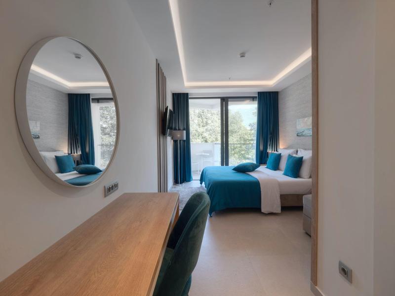 Modernes Schlafzimmer mit großem Bett, blauen Vorhängen, Spiegel und Holztisch vor dem Fenster.