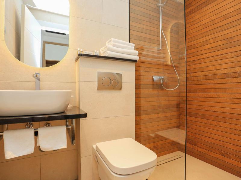 Kompaktes Bad mit Holzverkleidung, weißer Toilette, rundem Spiegel und Glasduschabtrennung.