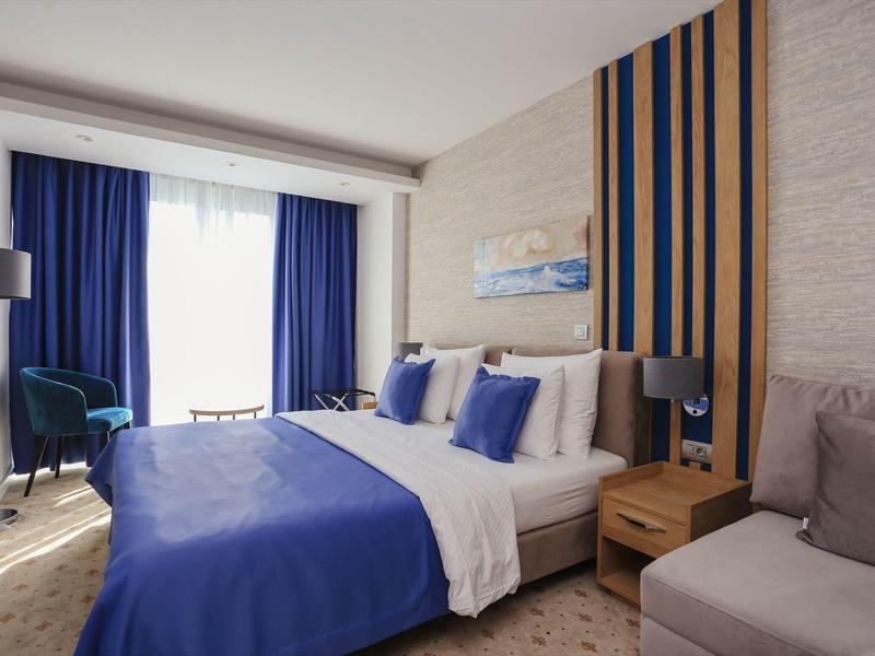 Gemütliches Schlafzimmer mit blauem Bett, Holzmöbeln und großem Fenster mit blauen Vorhängen.