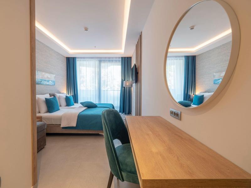 Modernes Hotelzimmer mit Doppelbett, Holztisch, rundem Spiegel und blauen Vorhängen.