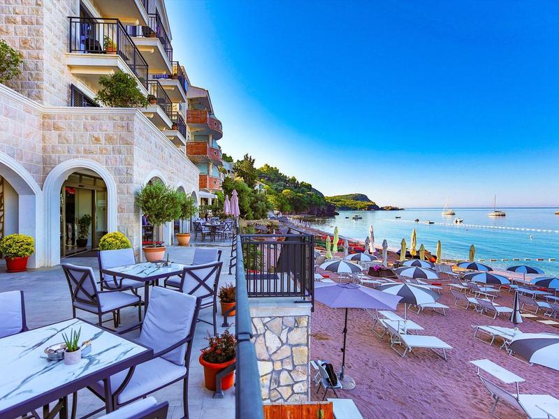 Strand mit Liegen und Sonnenschirmen neben einem weißen Gebäude und klarem blauem Himmel.