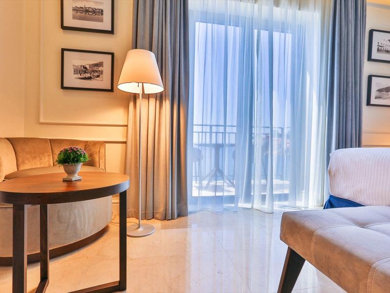 Helles Wohnzimmer mit großen Fenstern, hellem Holzboden, braunen Möbeln und blauen Vorhängen.