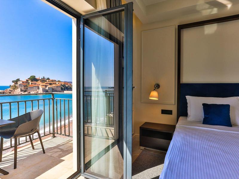 Hell eingerichtetes Zimmer mit Balkon, Meerblick, blauem Bett und modernem Balkonmöbel.