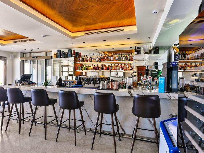 Moderner Barbereich mit schwarzem Tresen, hohen Stühlen und beleuchtetem Deckenakzent in warmem Orange.