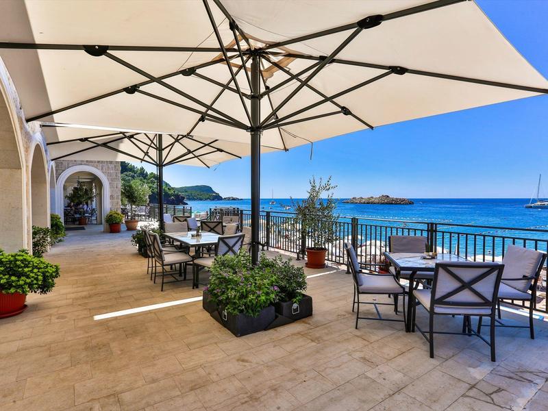 Terrassenbereich mit Sonnenschirmen, Tischen und Stühlen am Meer bei klarem Himmel.