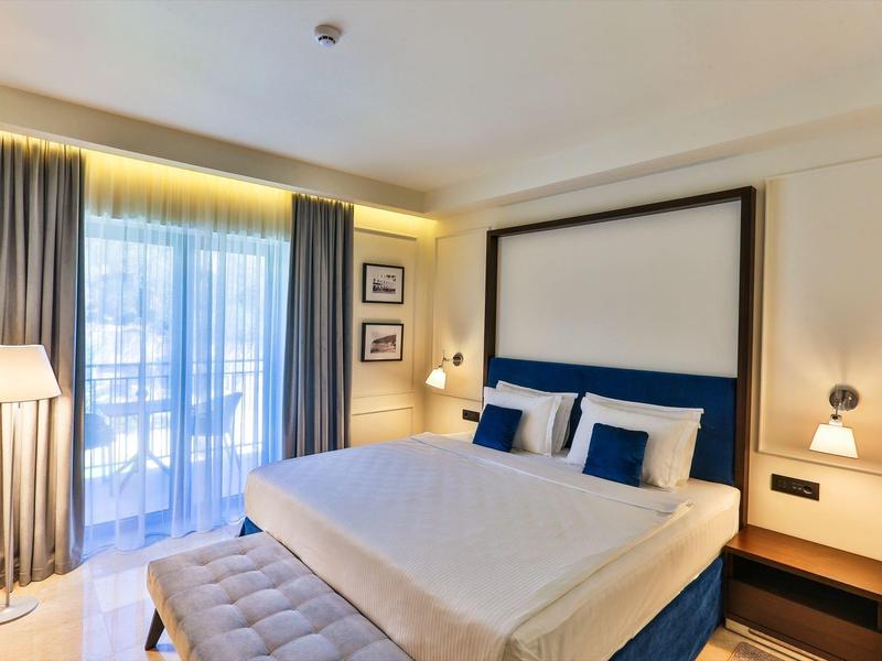 Modernes Schlafzimmer mit großem Bett, blauen Kissen, grauem Vorhang und heller Beleuchtung.